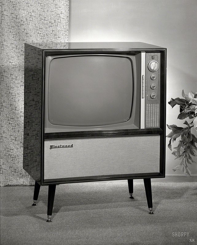 an old tv sitting on top of a wooden stand in front of a potted plant