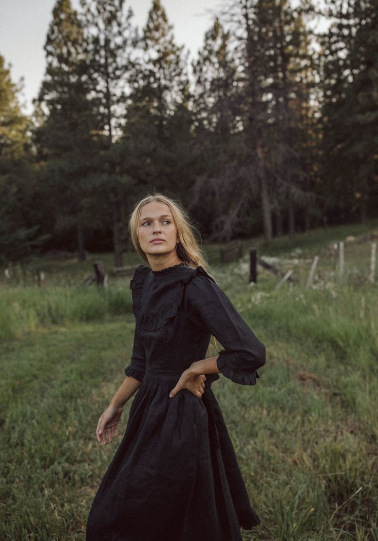 a woman in a black dress is standing in the grass with her hands on her hips