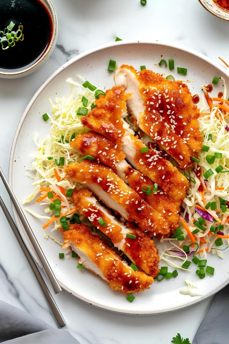 a white plate topped with chicken and coleslaw next to chopsticks on a table