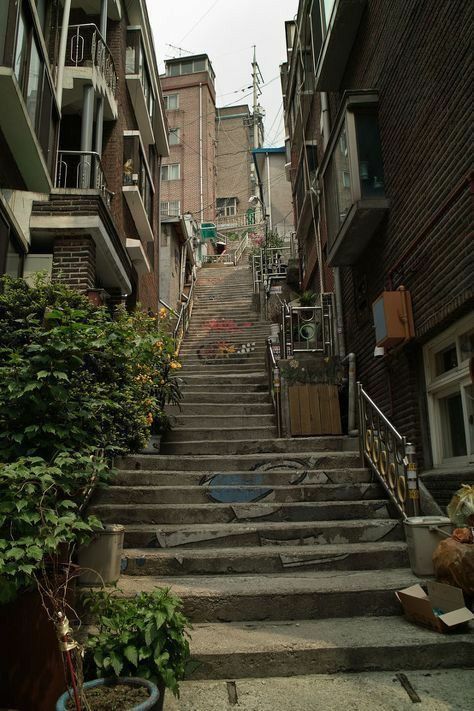 an alleyway with steps leading up and down to apartment buildings on either side, surrounded by greenery