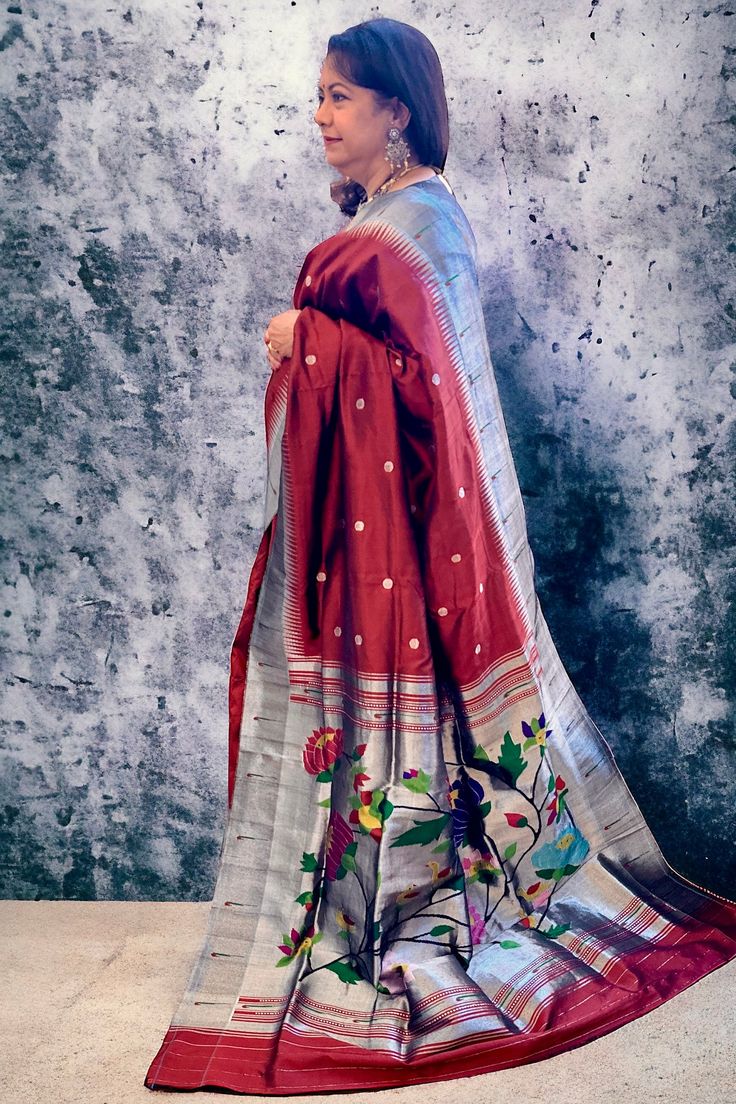 This exquisite regal paithani saree is handwoven in deep burgundy color. Silver zari dollar buttis adorn the body while the silver zari border is decorated with handwoven in muniya border. The elaborate pallu is woven with colorful lotus along with winding vines. The saree comes with plain blouse with matching borders. Approximate Length 6.5 mtrs (inclusive of blouse length)Height - 48- 52" Saree comes with fall, picot and tassels done. Blouse piece is cut. Approximate weight - 1.8 lbs Kindly Note : The colors you see on your device may vary due to the color reproduction, brightness and resolution of individual devices. If you'd like more clarity before your purchase, please contact our support team. Bollywood Style Burgundy Traditional Wear With Pallu, Burgundy Traditional Wear With Zari Work For Festivals, Traditional Silver Silk Saree, Traditional Burgundy Dupatta With Pallu, Burgundy Traditional Wear With Pallu For Festivals, Traditional Burgundy Saree For Festive Occasions, Festive Burgundy Traditional Wear With Pallu, Transitional Paithani Silk Saree With Weaving Work, Festive Burgundy Saree With Pallu Detail