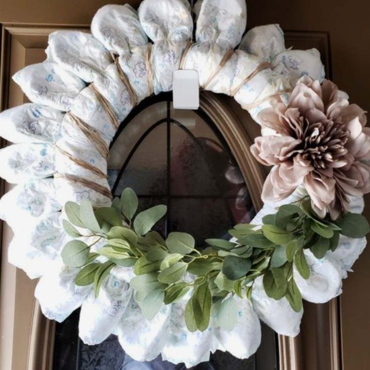 a wreath with flowers and leaves hanging on the front door