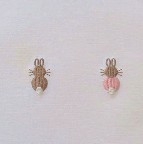 three small embroidered bugs sitting on top of a white surface, one pink and one brown