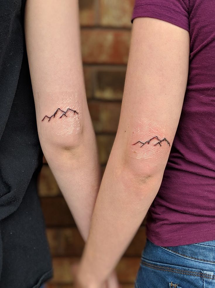 two people holding hands with tattoos on their arms