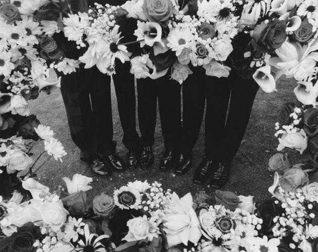 black and white photograph of four men in tuxedos with flowers around their necks