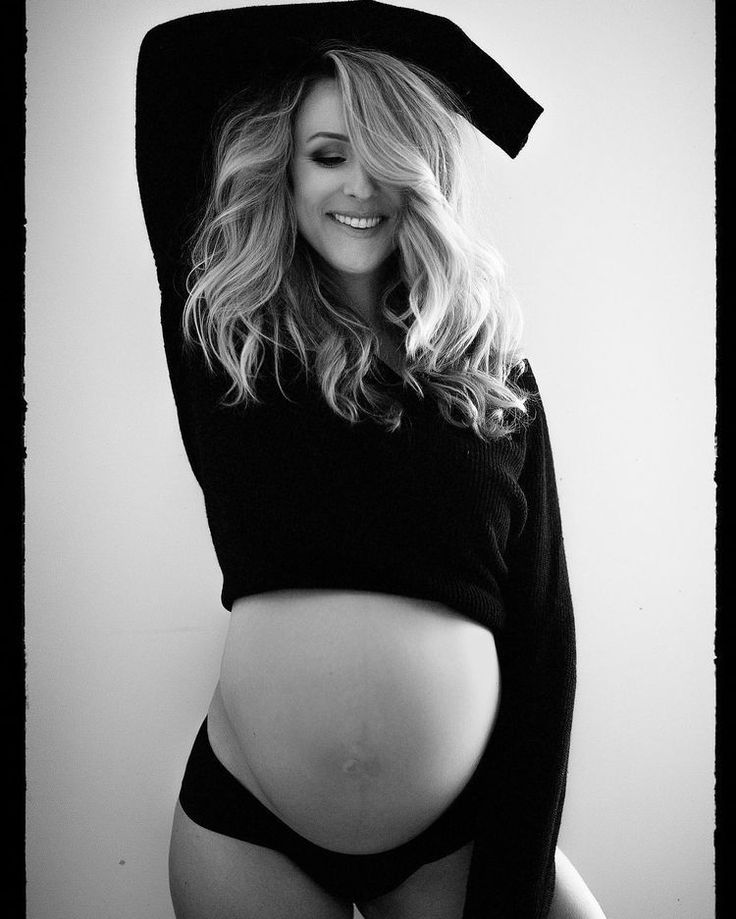 a pregnant woman wearing a hoodie and panties poses for a black and white photo