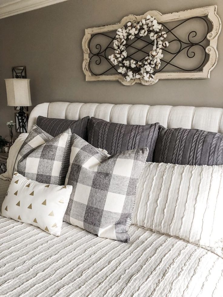 a white bed topped with pillows next to a wall mounted sign and a wreath on top of the headboard