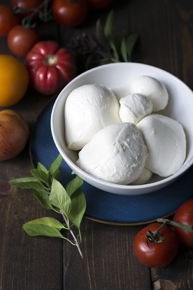 a bowl filled with mozzarella sitting on top of a table next to tomatoes