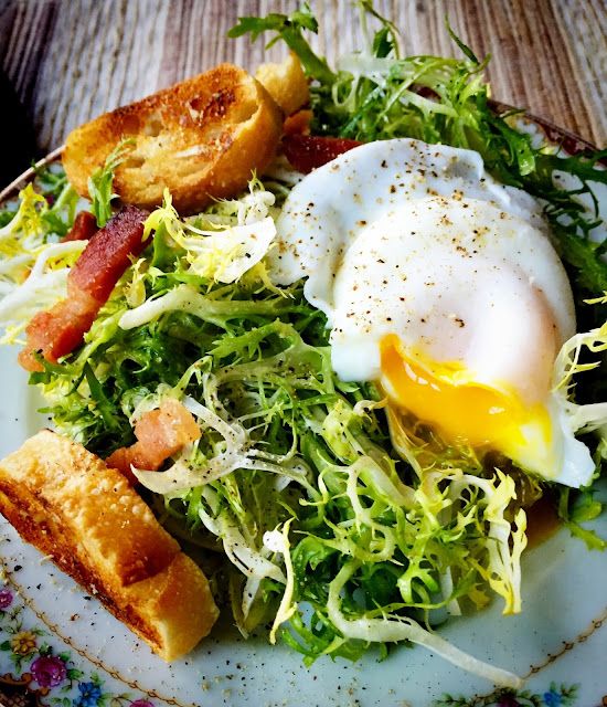 a white plate topped with salad and an egg on top of toasted croutons