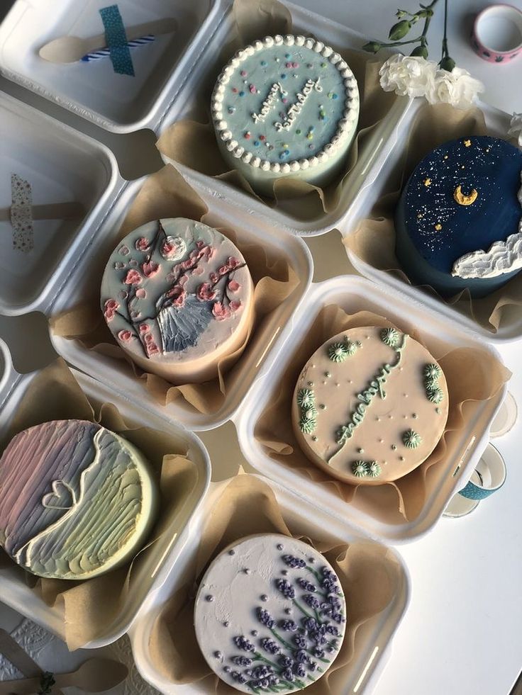 six decorated cupcakes in plastic containers on a table