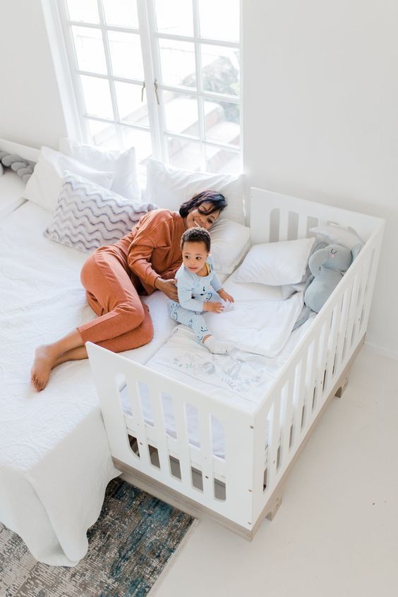 a woman laying on top of a bed next to a baby in a crib