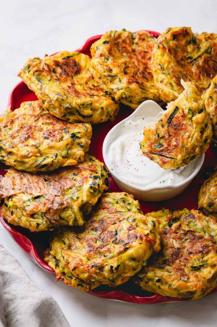 several crab cakes on a red platter with a small bowl of ranch dressing in the middle