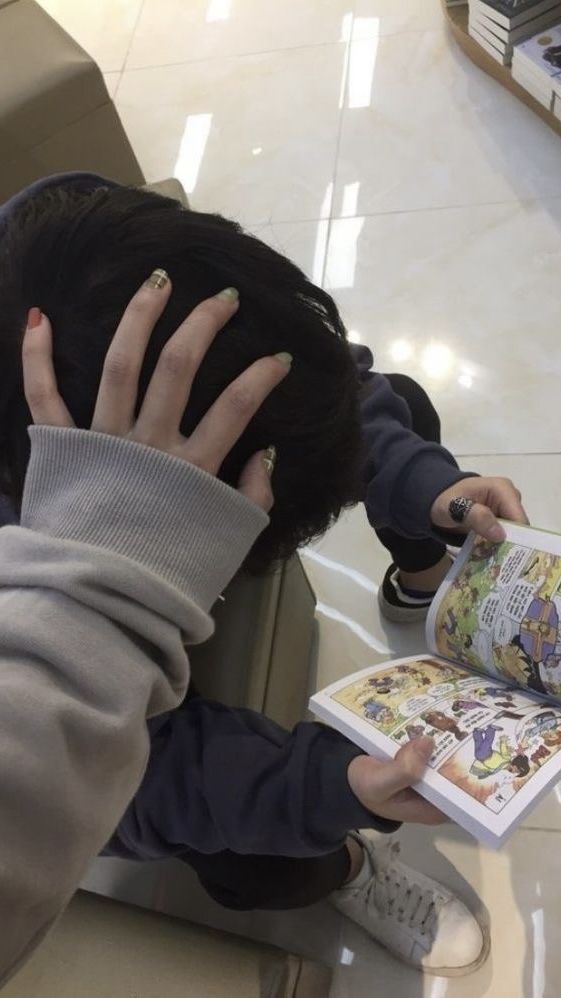 a person sitting at a table reading a book with their hands on top of the book