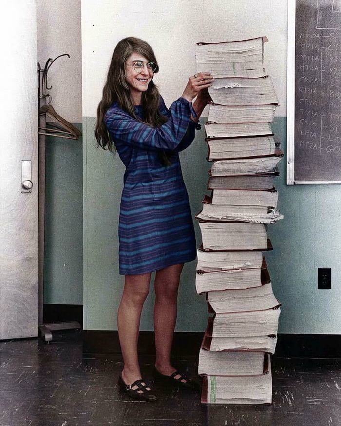 a woman standing next to a stack of papers