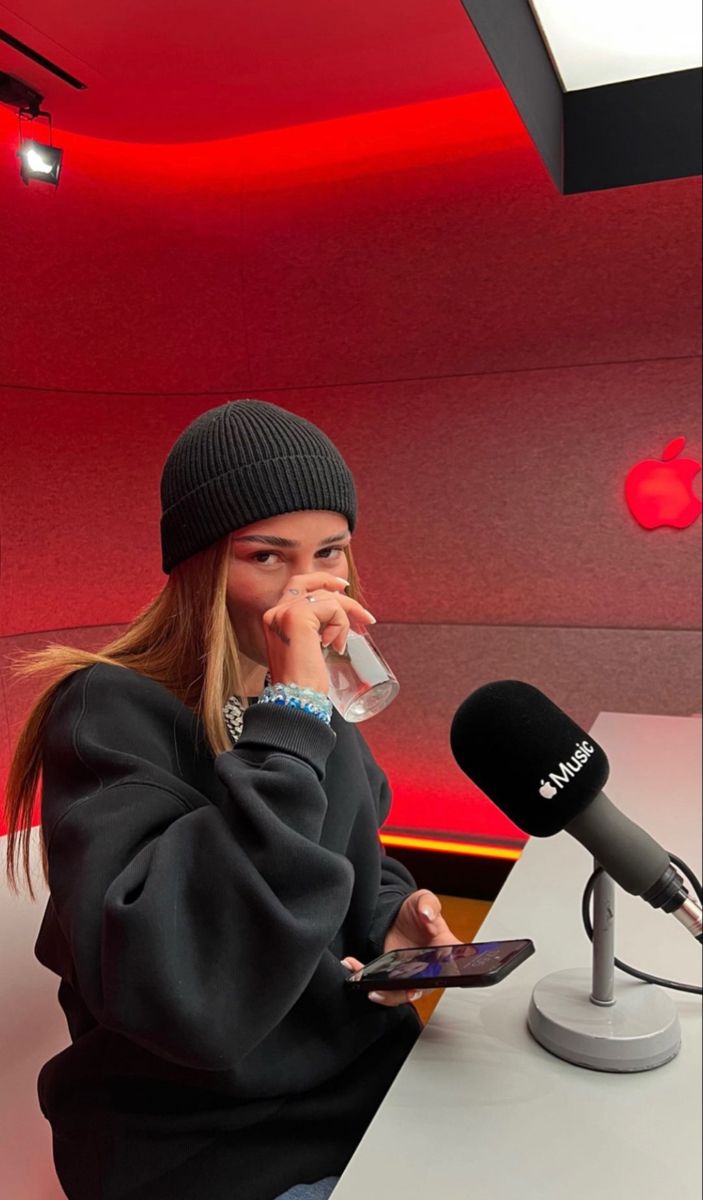 a woman sitting in front of a microphone holding a tablet computer and talking on the phone