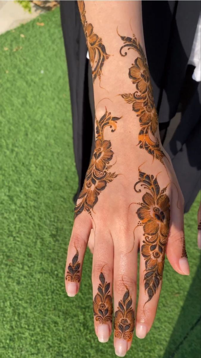 a woman's hand with hennap on it and green grass in the background