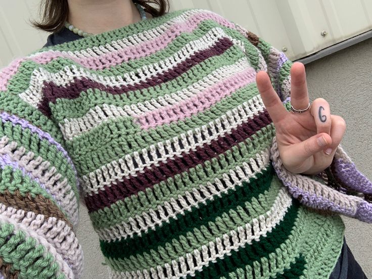 a woman is making the peace sign with her hand while wearing a crocheted sweater