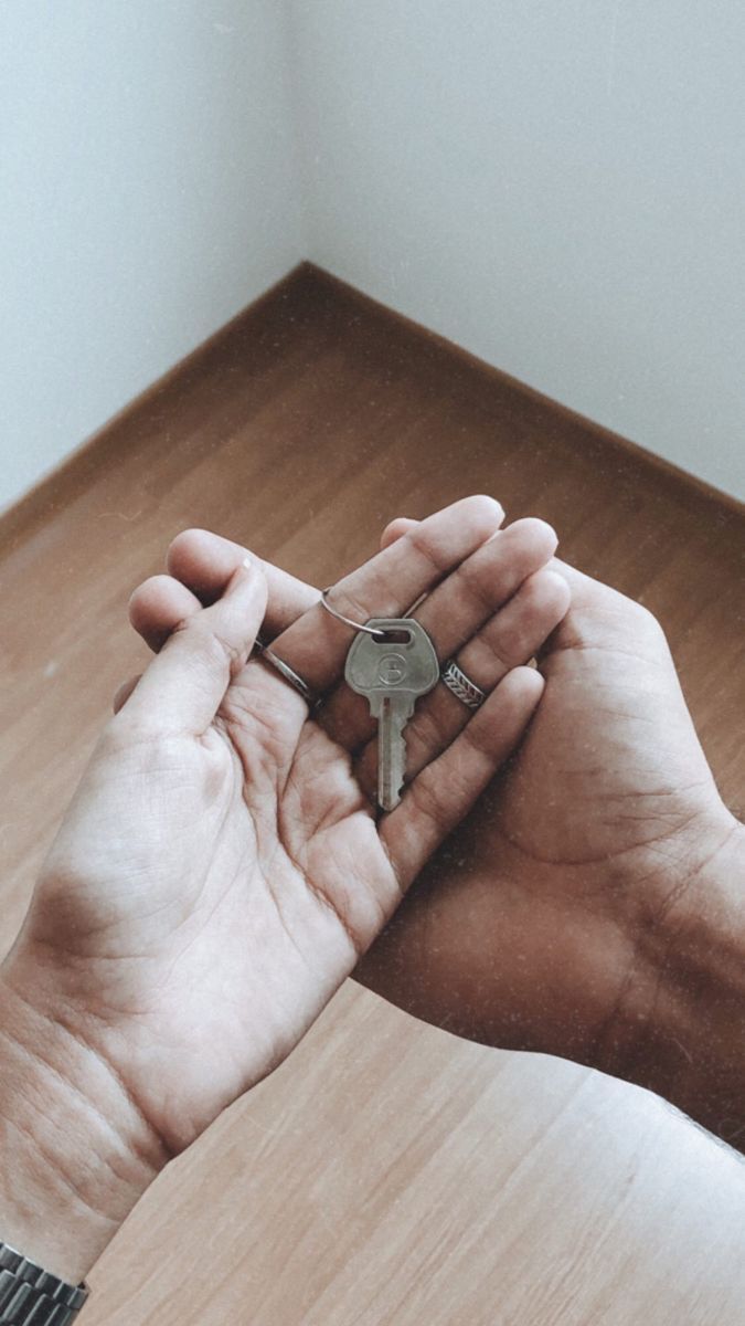 a person holding a key in their hand on top of a wooden floor next to a window