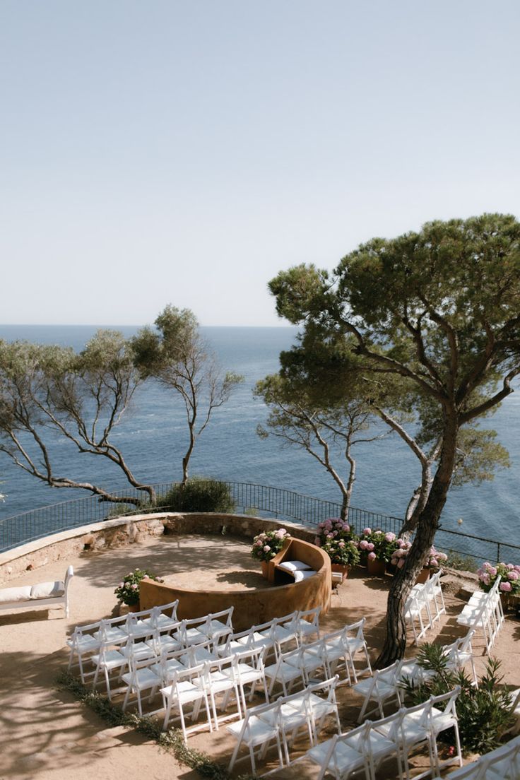 an outdoor ceremony set up with white chairs and flowers on the ground, overlooking the ocean