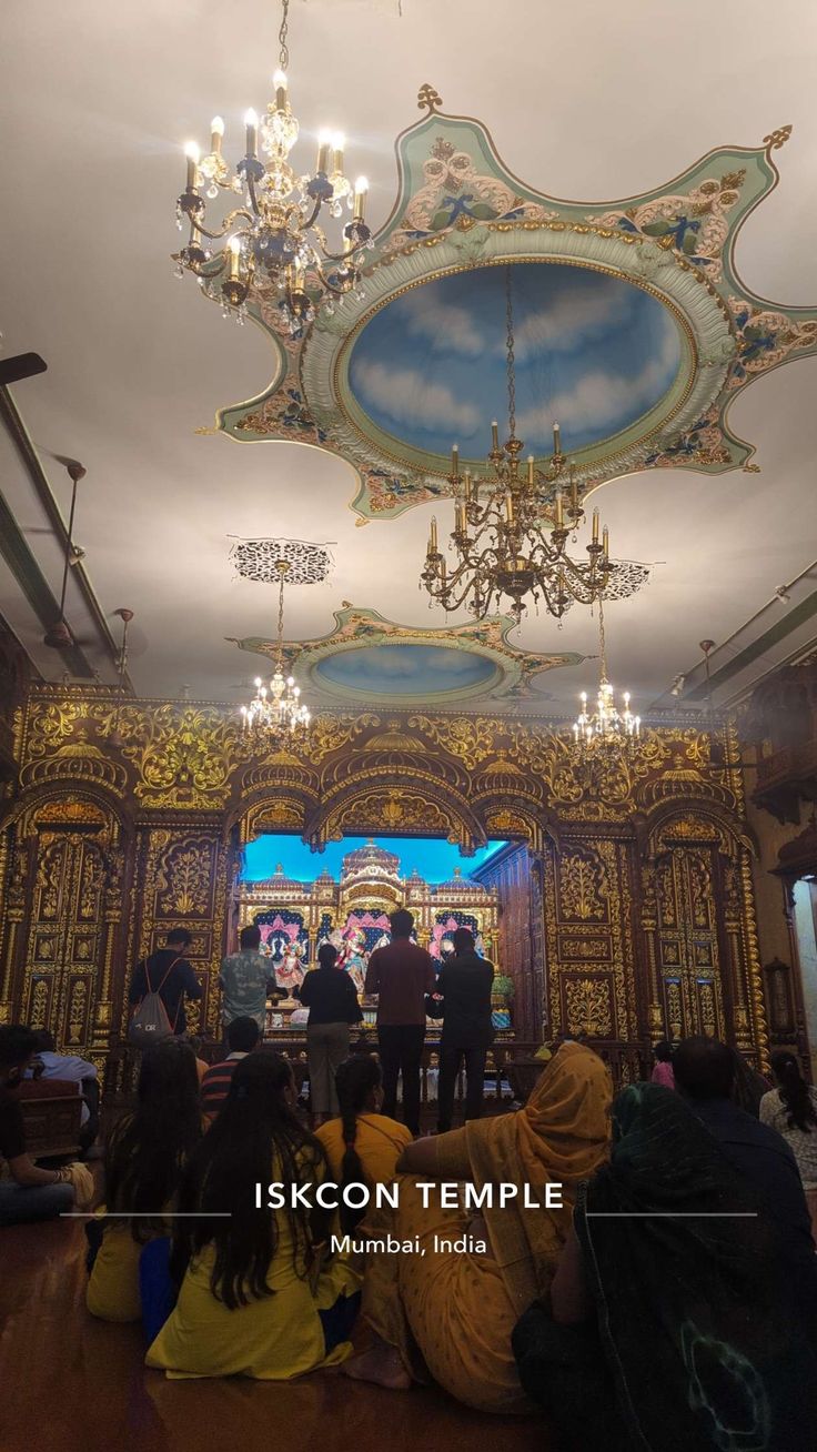 people sitting on the floor in front of a stage with chandeliers and paintings