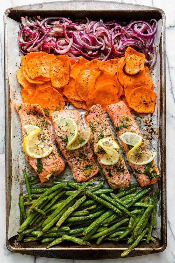 salmon and vegetables on a baking sheet with lemons, onions, carrots, green beans