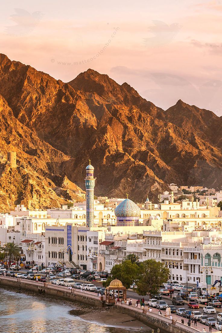 a city with mountains in the background and cars parked on the street below it,