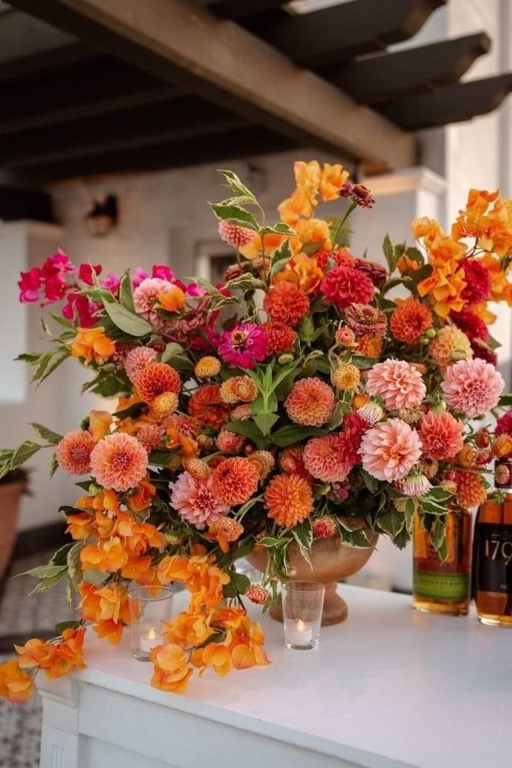 an arrangement of flowers in vases sitting on a table with two bottles of booze