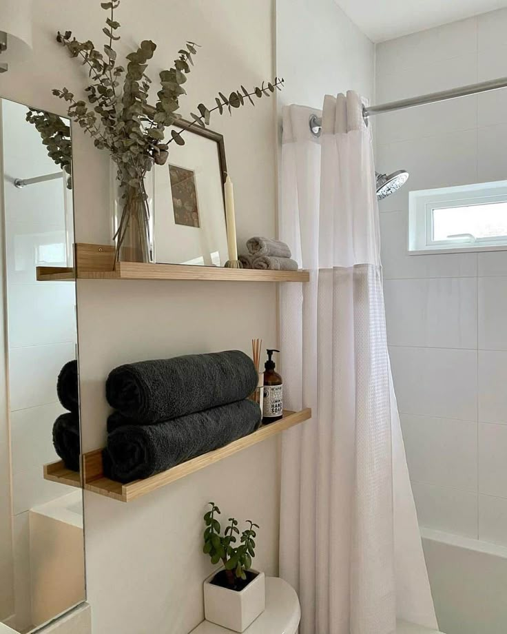 a white bathroom with black towels and plants on the shelf above the shower curtain, along with toiletries