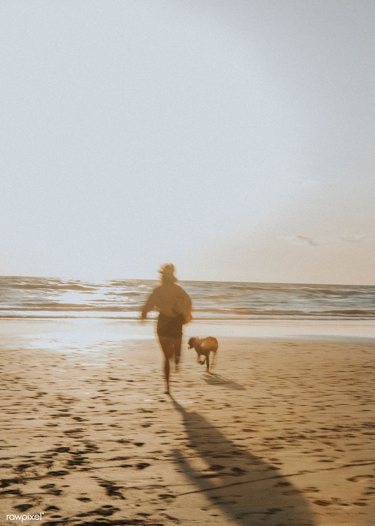 a person running on the beach with a dog next to him and an ocean in the background