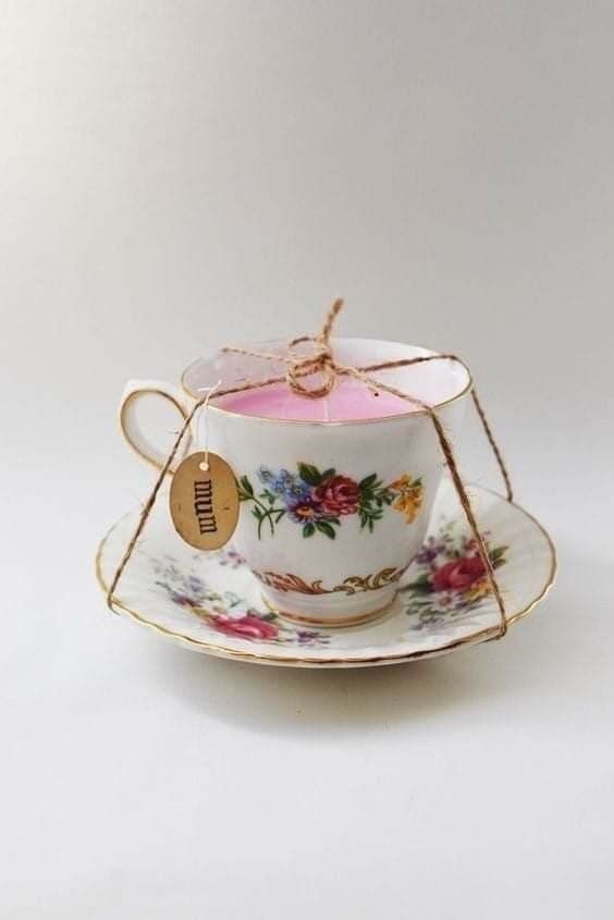 a tea cup and saucer with a pink candle in the middle on a white background