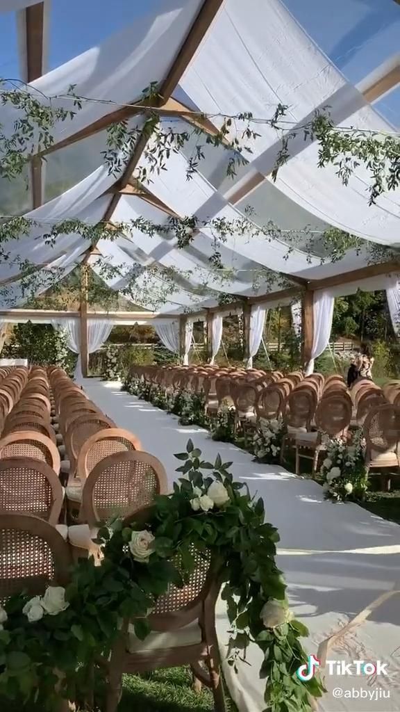 an outdoor wedding venue set up with white drapes and greenery on the ceiling