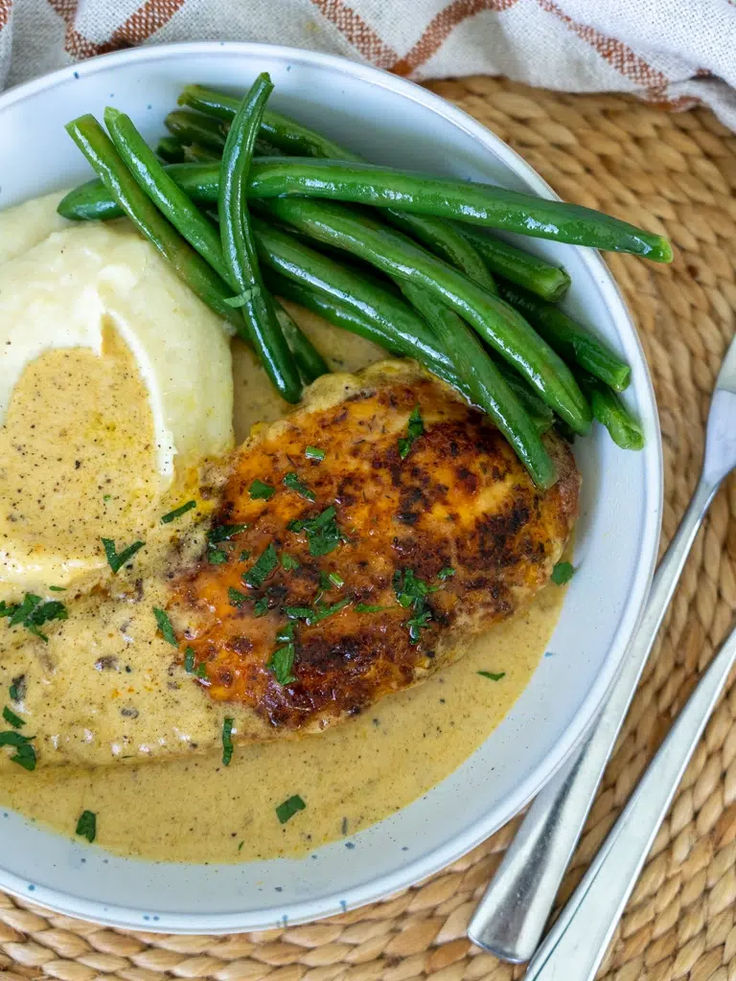 a white plate topped with meat covered in gravy and mashed potatoes next to green beans