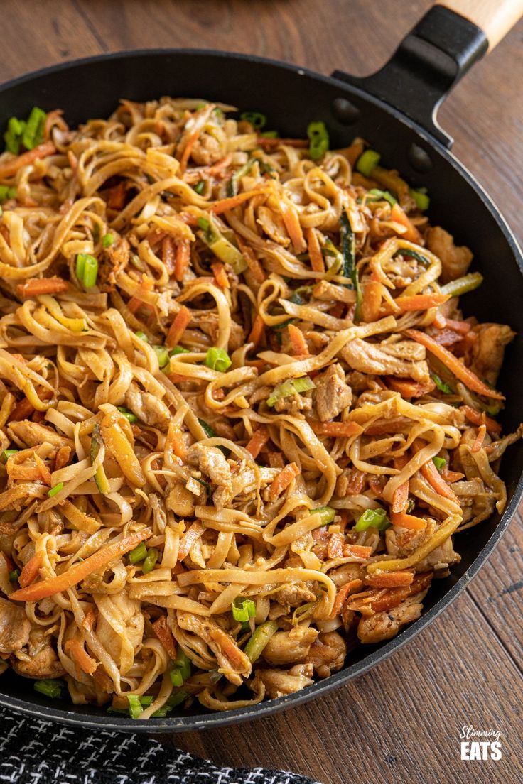 a pan filled with noodles and vegetables on top of a wooden table