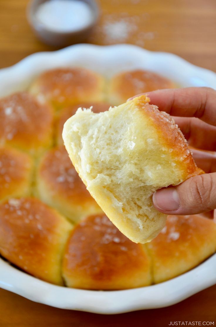 a person holding a piece of bread in front of a bowl full of buns