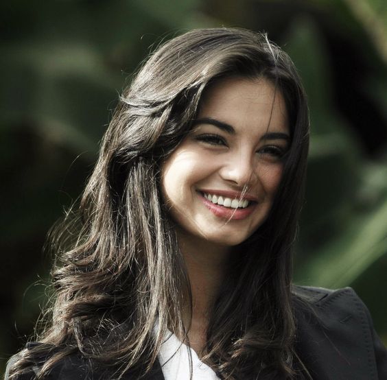 a woman with long hair smiling and wearing a black blazer over a white shirt