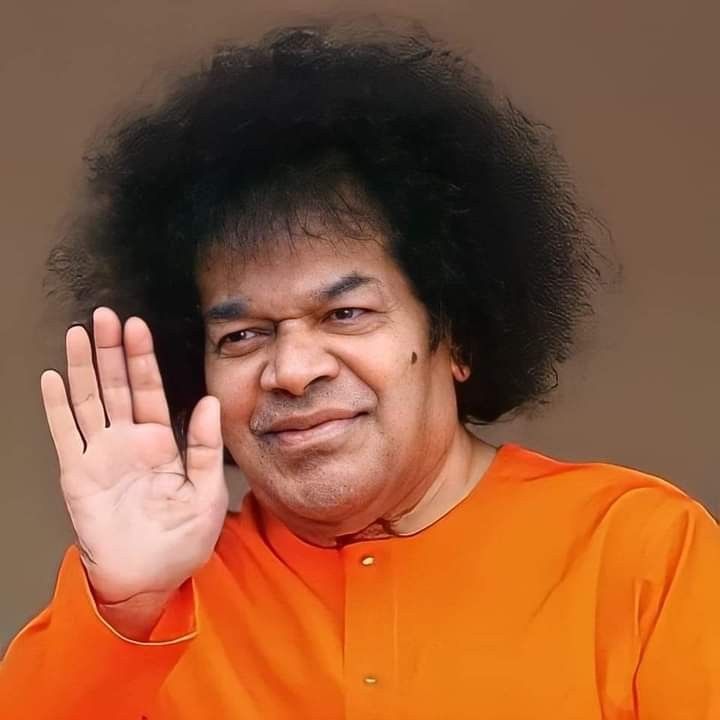 a man with an afro waves to the camera while wearing an orange shirt and holding his hand up in front of him