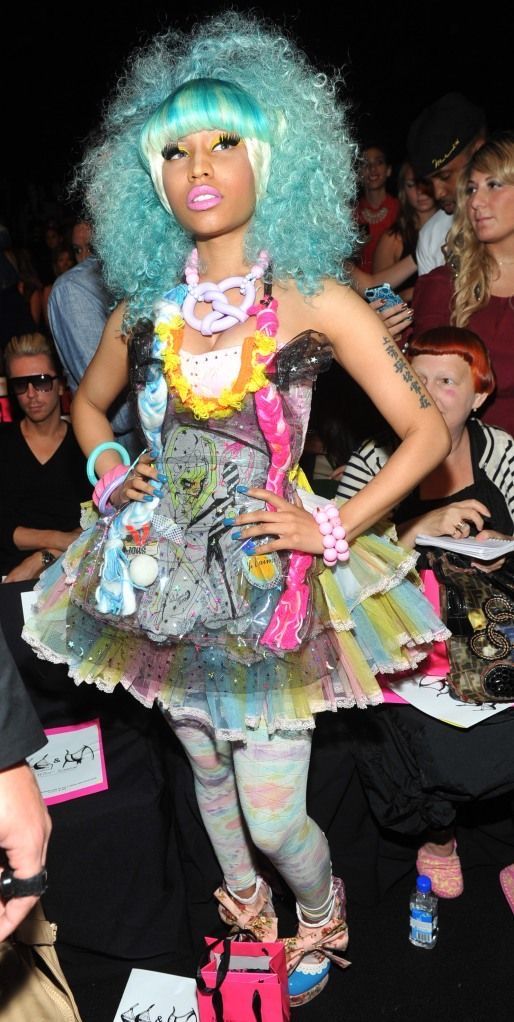 a woman with blue hair wearing a dress and shoes at a fashion show in front of a crowd