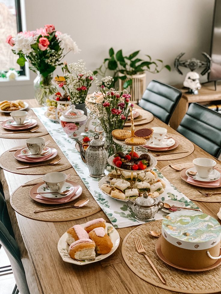 a long table with plates and cups filled with pastries on it next to flowers