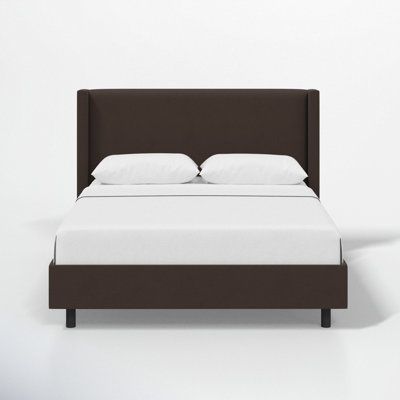 a bed with white sheets and brown headboard against a white wall in an empty room