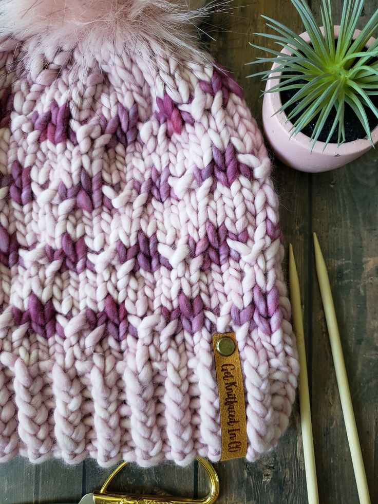 a pink and purple knitted hat next to some knitting needles