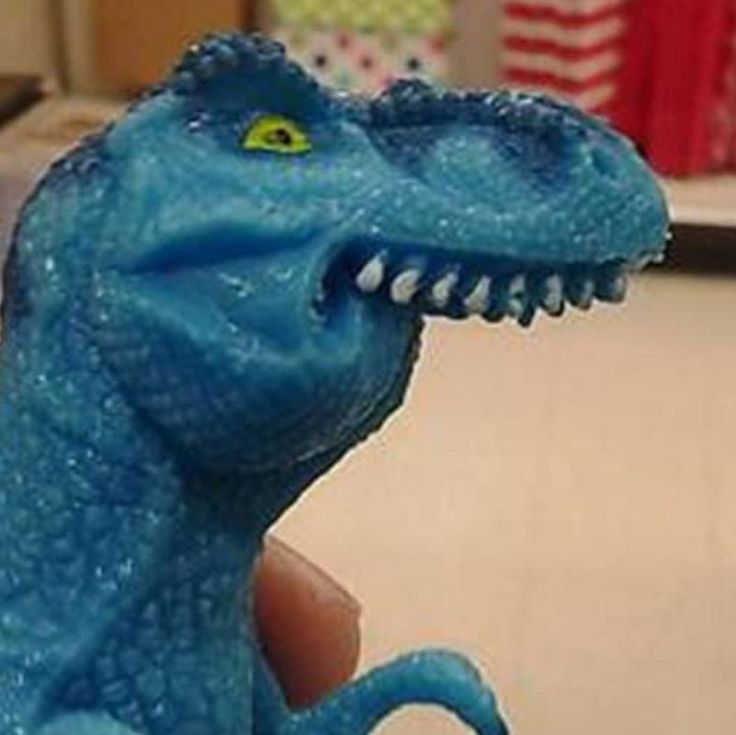 a blue toy dinosaur is being held in the palm of someone's left hand