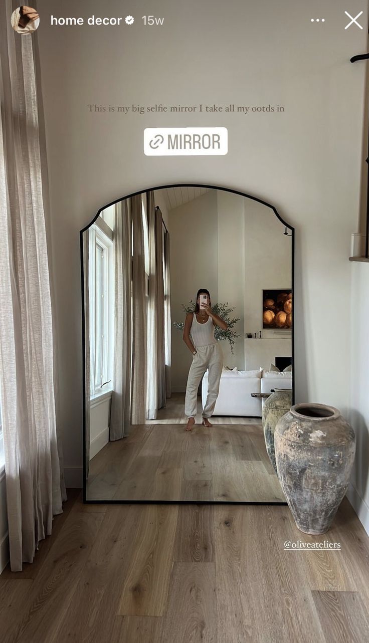 a woman standing in front of a mirror with her reflection on the floor next to a vase