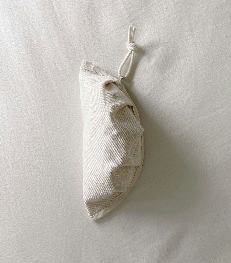 a white bag is laying on top of a plain linen material bed sheet with a knot at the end