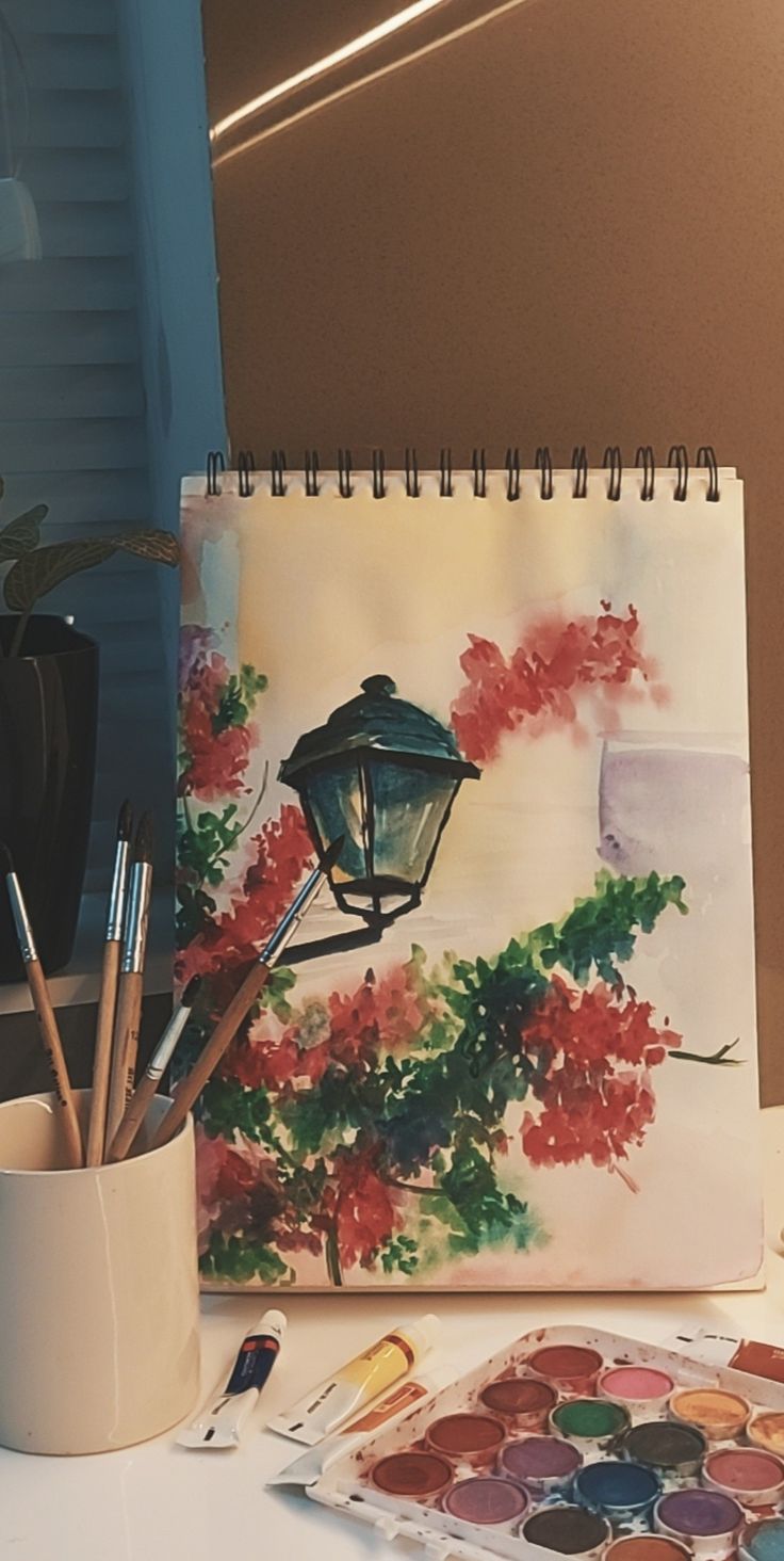 a painting and paintbrushes on a table next to a vase with watercolors