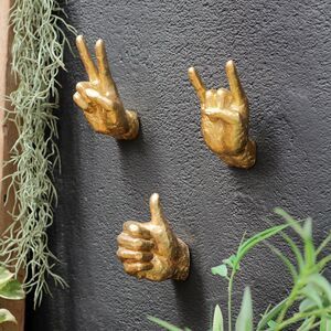 three gold hand - shaped hooks on the side of a wall with plants growing in it