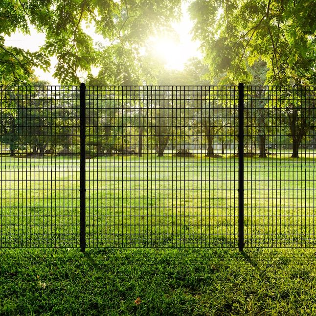 a black fence in the middle of a grassy field with trees and grass behind it