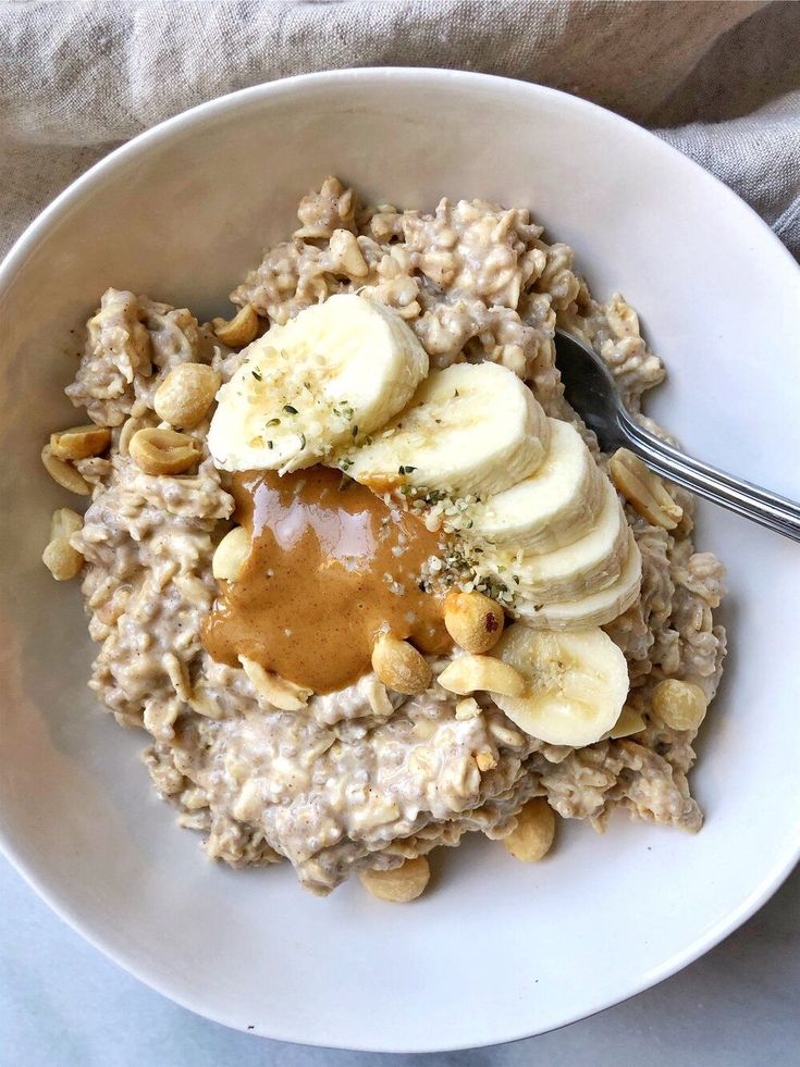 a bowl of oatmeal with bananas and peanut butter on top is being held by a person