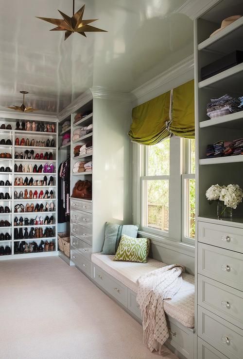 a walk in closet with lots of shoes on the shelves and window seat next to it