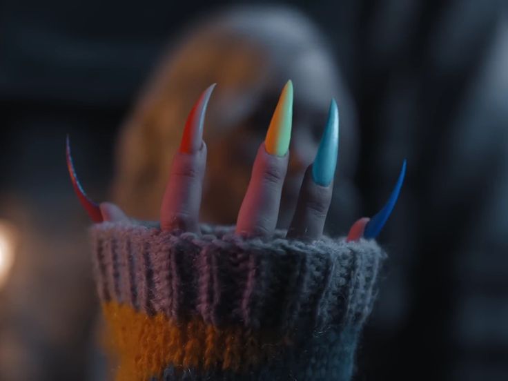 a person with multicolored nails holding their fingers up to the camera while wearing a knitted sweater