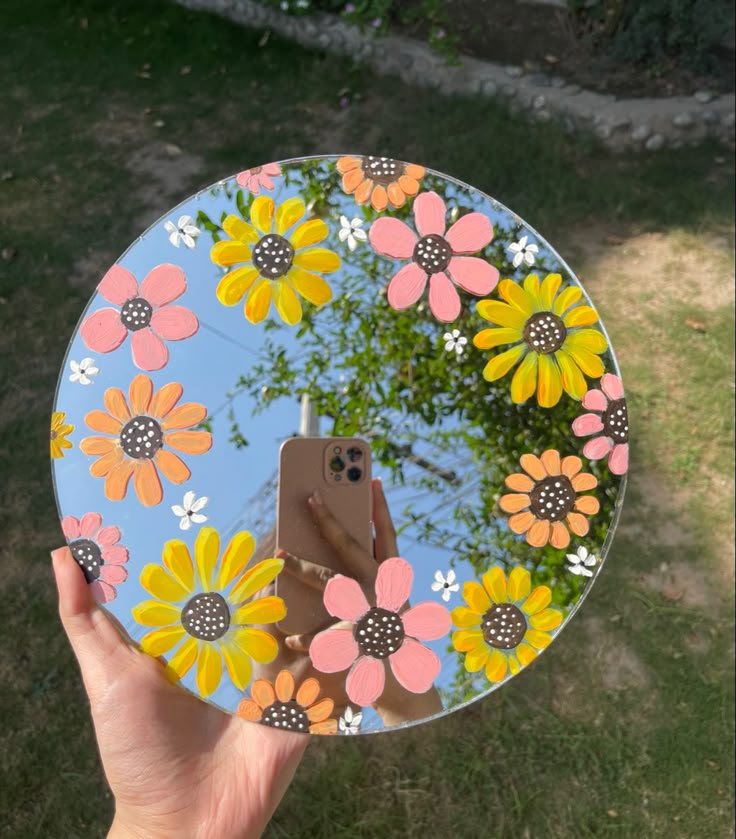 a person holding up a phone in front of a mirror with flowers painted on it